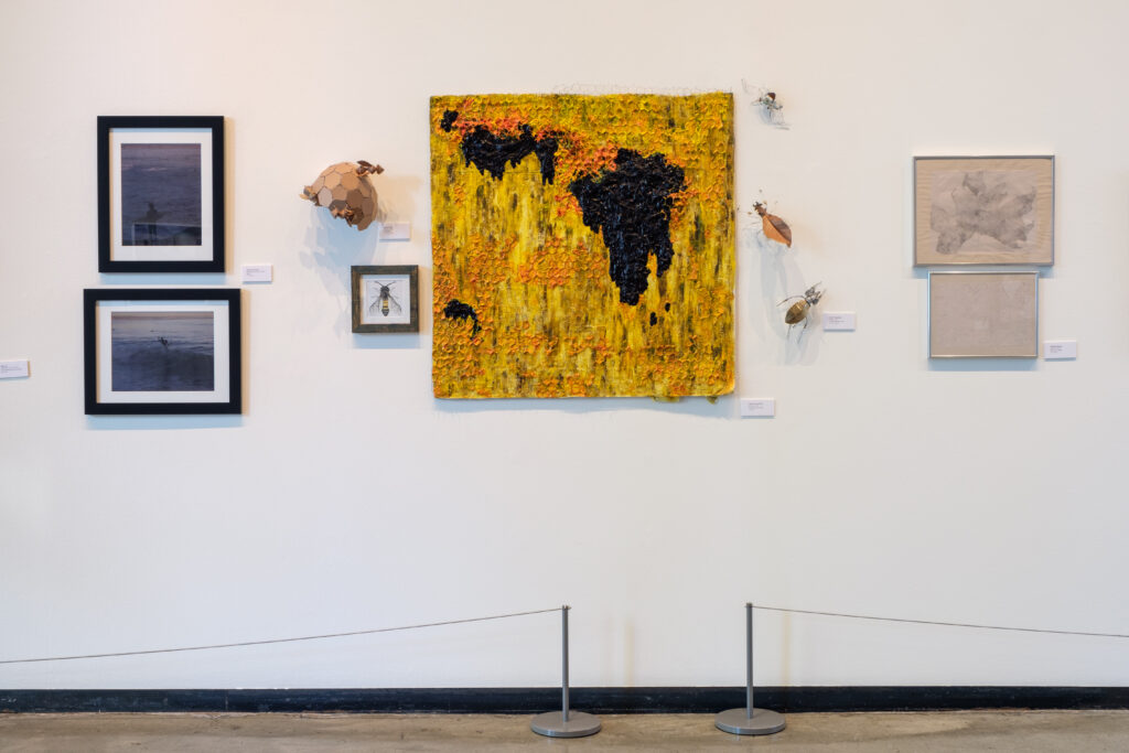large yellow painting surrounded by smaller paintings hung on a white gallery wall