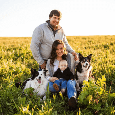 image of white woman, man and their baby with 2 dogs sitting in a field