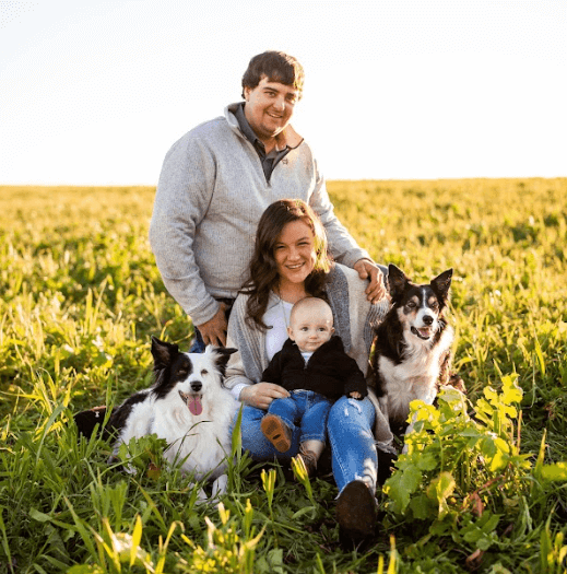 image of white woman, man and their baby with 2 dogs sitting in a field