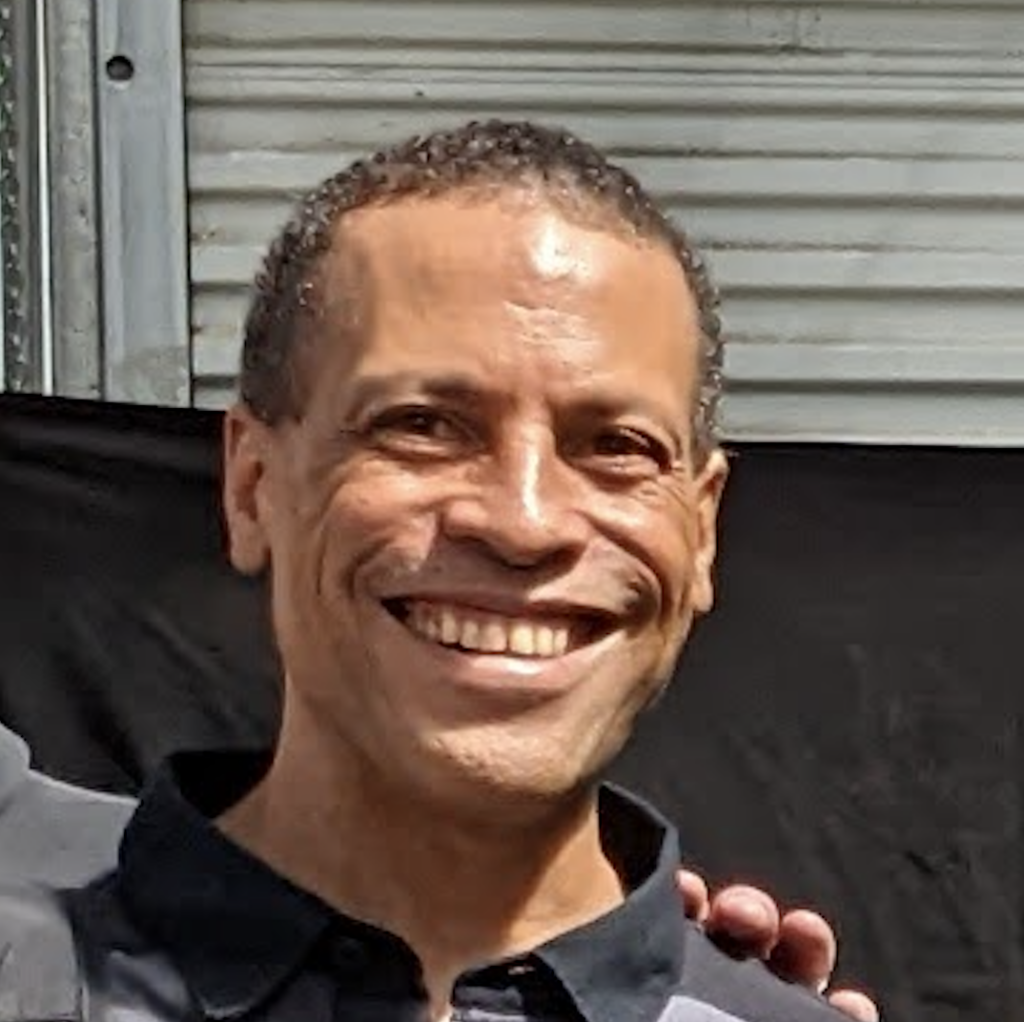 light skinned, black man where black collared shirt against light gray and dark gray background